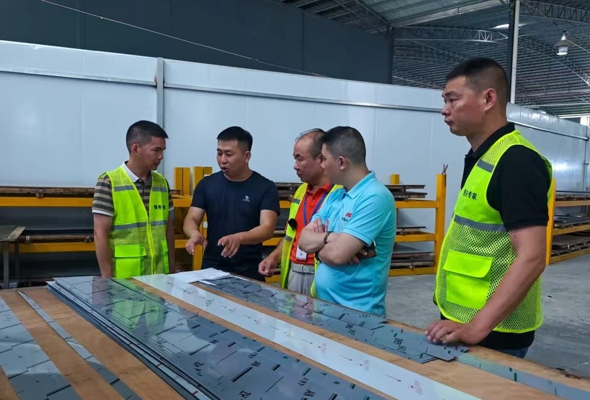 Safety engineers reviewing machine guarding arrangements with plant management on a sheet-metal shop floor, with formed panels laid out in the foreground